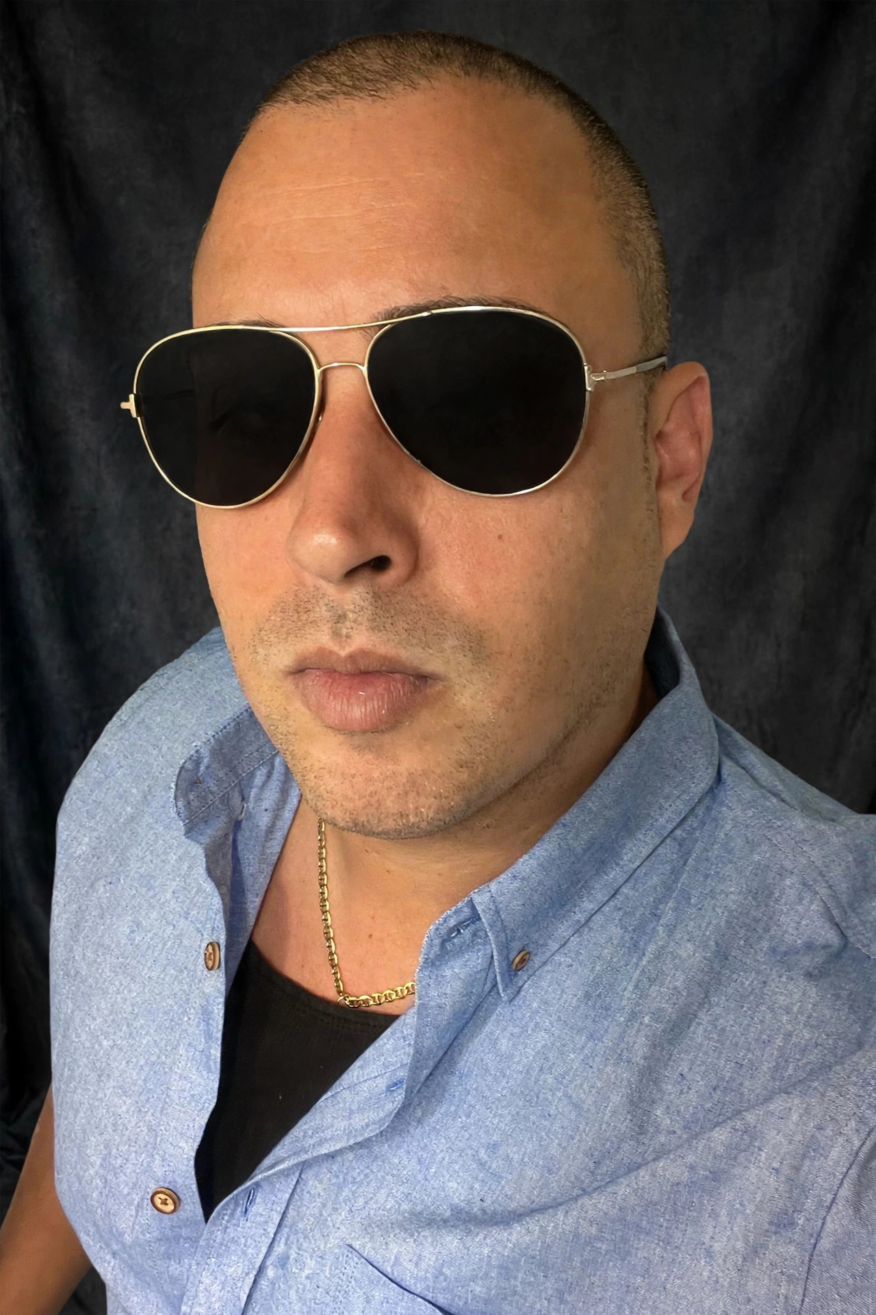 Messy Jordan press portrait, gold aviator sunglasses against a black backdrop